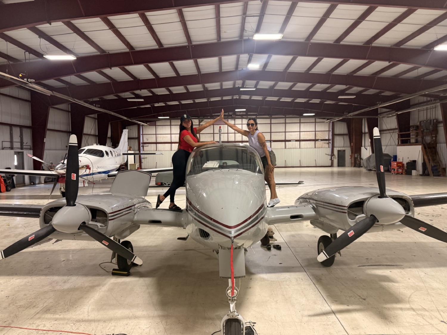 Two pilots reaching across the nose of the aircraft in the hangar