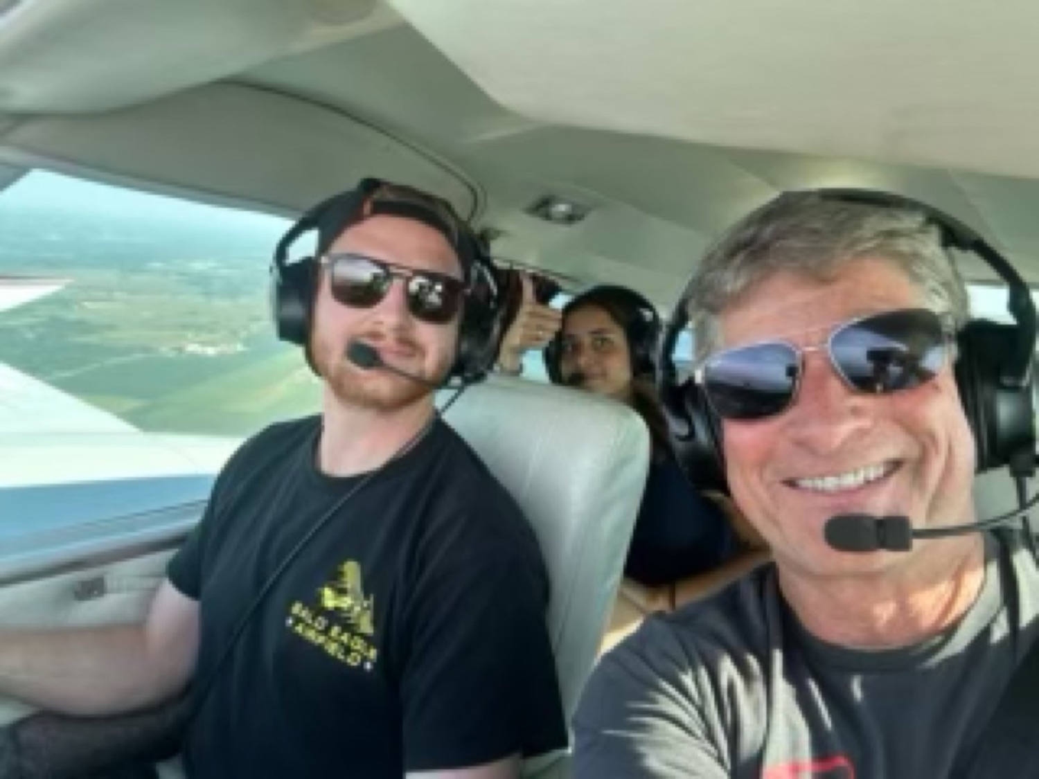 Three people in headsets in the cockpit with the wing and ground visible